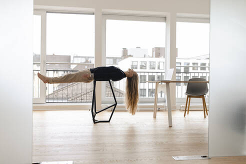 Young businesswoman practicing yoga in office lying on a stool - GUSF03257