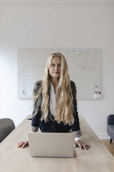 Portrait of young businesswoman practicing yoga on desk in office - GUSF03258