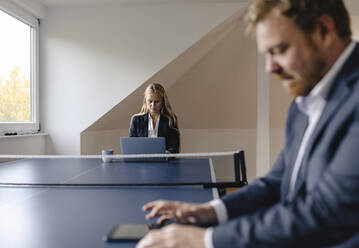Geschäftsmann und Geschäftsfrau arbeiten an einer Tischtennisplatte im Büro - GUSF03261