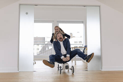 Playful businesswoman pushing businessman on toy car in office - GUSF03280