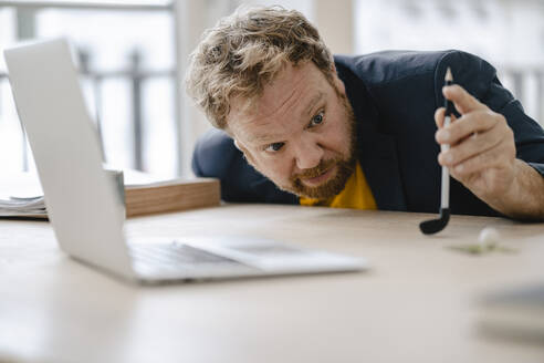 Geschäftsmann spielt Golf auf dem Schreibtisch im Büro - GUSF03294