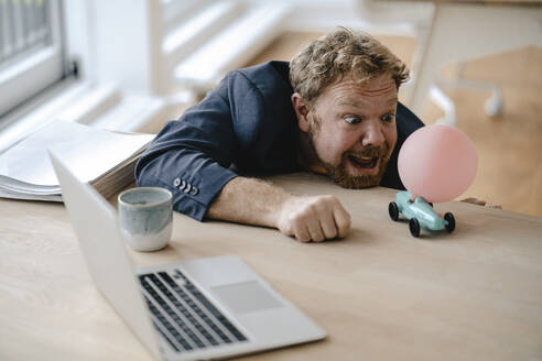 Businessman playing with miniature toy car on desk in office - GUSF03296