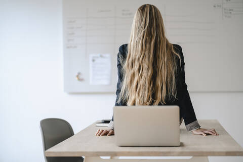 Rückansicht einer jungen Geschäftsfrau beim Turnen auf dem Schreibtisch im Büro, lizenzfreies Stockfoto