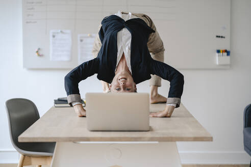 Young businesswoman practicing yoga on desk in office - GUSF03312