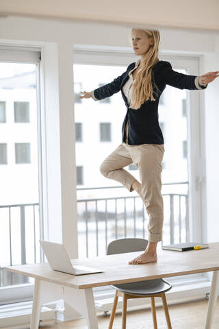 Junge Geschäftsfrau übt Yoga auf dem Schreibtisch im Büro, lizenzfreies Stockfoto