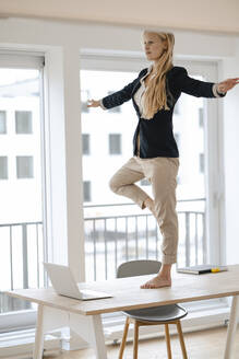 Young businesswoman practicing yoga on desk in office - GUSF03313