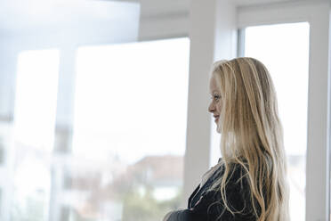 Smiling young businesswoman at the window in office - GUSF03340