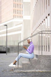 Porträt einer weißhaarigen Frau mit weißen Kopfhörern beim Musikhören in der Stadt - AFVF05018