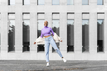 White haired woman with white headphones listening to music and dancing in the city - AFVF05027