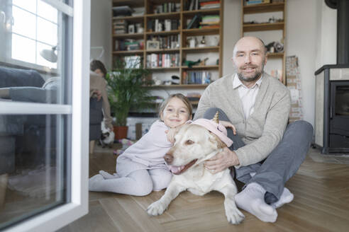 Porträt eines Vaters, der mit seiner kleinen Tochter und dem Hund zu Hause auf dem Boden sitzt - KMKF01201