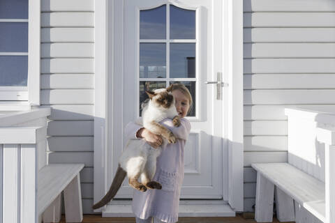 Kleines Mädchen, das eine Katze auf dem Arm trägt, vor einem Hauseingang, lizenzfreies Stockfoto