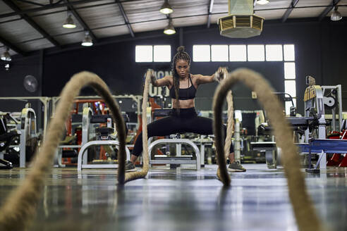 Weibliche Athletin beim Krafttraining mit schweren Seilen im Fitnessstudio - VEGF01480