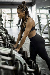 Weibliche Athletin wählt Gewichte für das Training im Fitnessstudio - VEGF01483