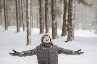 Porträt eines Jungen, der im Winterwald Schneeflocken fängt - EYAF00838