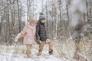 Zwei Geschwister spazieren Hand in Hand im Winterwald - EYAF00841