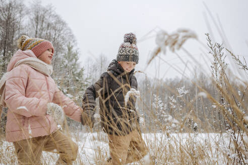 Zwei Geschwister spazieren Hand in Hand im Winterwald - EYAF00842
