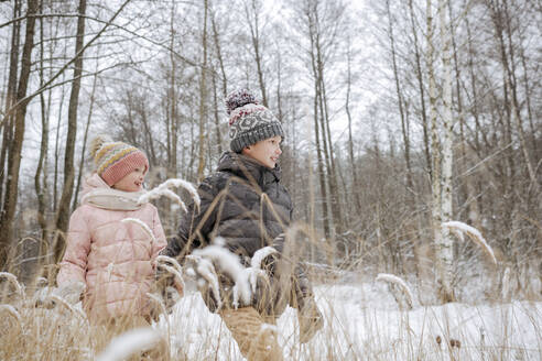 Two siblings walking hand in hand in winter forest - EYAF00843