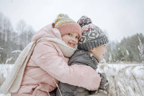 Junge, der seine kleine Schwester im Winterwald huckepack nimmt - EYAF00844
