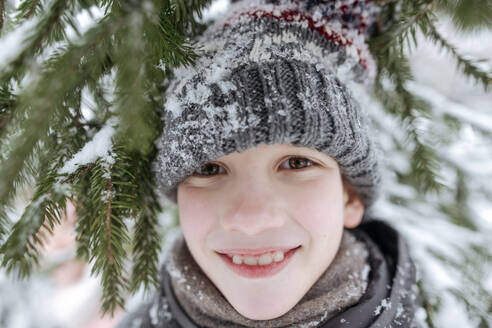 Porträt eines lächelnden Jungen, der im Winterwald Spaß hat - EYAF00850