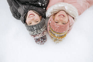 Portrait of two smiling siblings lying on snow - EYAF00851