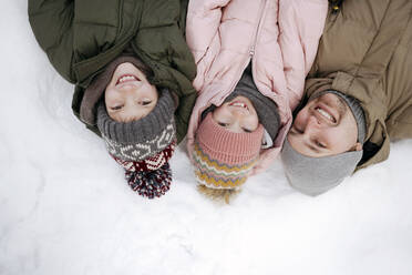 Familienporträt von Vater und zwei Kindern, die im Schnee liegen - EYAF00856