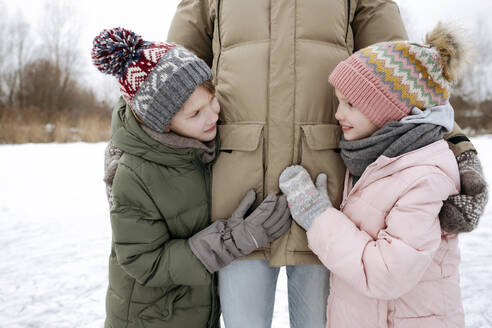 Zwei lächelnde Geschwister zusammen mit ihrem Vater im Winter - EYAF00859