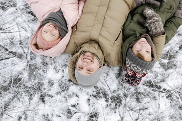 Familienporträt von Vater und zwei Kindern auf dem Eis liegend im Winter - EYAF00860