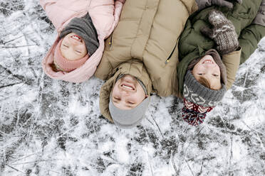 Family portrait of father and two children lying on ice in winter - EYAF00860