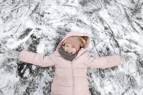 Porträt eines glücklichen Mädchens mit ausgestreckten Armen auf Eis liegend, lizenzfreies Stockfoto