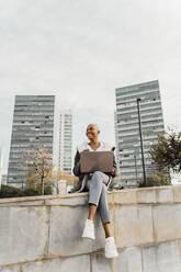 Casual businesswoman sitting in the city, using laptop - AFVF05072