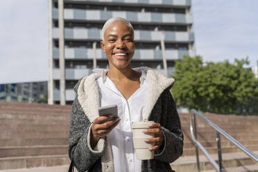 Stylish businesswoman commuting in the city, carrying smartphone and coffee cup - AFVF05078