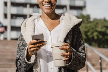Stilvolle Geschäftsfrau beim Pendeln in der Stadt, mit Smartphone und Kaffeetasse - AFVF05079