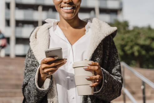 Stylish businesswoman commuting in the city, carrying smartphone and coffee cup - AFVF05079