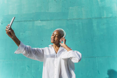 Schöne Frau steht vor einer blaugrünen Wand, hört Musik und macht Selfies - AFVF05094