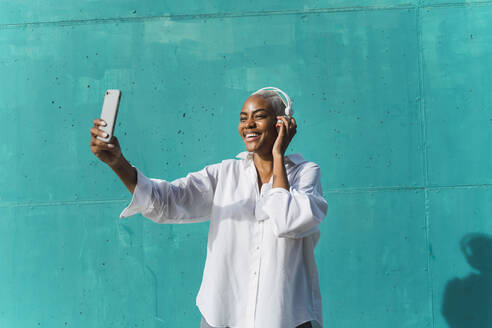 Beautiful woman standing in front of teal wall, listening music, taking selfies - AFVF05095