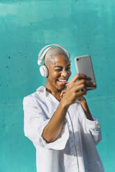 Schöne Frau steht vor einer blaugrünen Wand, hört Musik und macht Selfies - AFVF05096