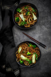 Overhead view of two bowls of soba noodles with pak choi and broccoli, soy sauce and black sesame - LVF08543
