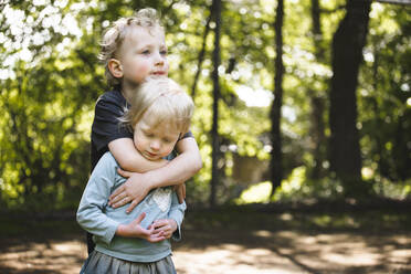Junge, der seine kleine Schwester im Freien umarmt - IHF00264