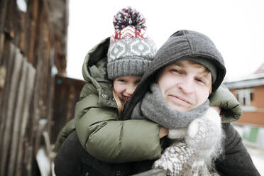 Porträt eines Vaters, der seine Tochter im Winter im Freien huckepack trägt - EYAF00864