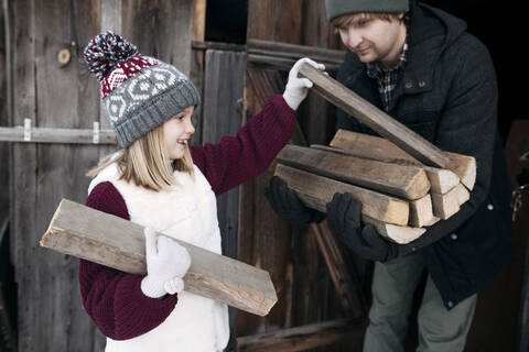 Tochter gibt ihrem Vater im Winter Brennholz, lizenzfreies Stockfoto