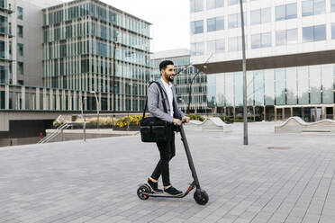 Casual young businessman riding electric scooter in the city - JRFF03965