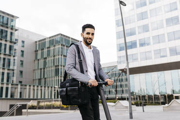 Portrait of casual young businessman with electric scooter in the city - JRFF03966