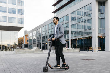 Casual young businessman riding electric scooter in the city - JRFF03967