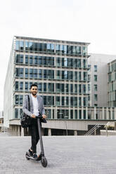 Portrait of casual young businessman with electric scooter in the city - JRFF03968