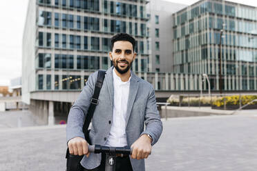 Portrait of casual young businessman with electric scooter in the city - JRFF03969