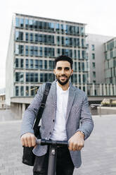 Portrait of casual young businessman with electric scooter in the city - JRFF03970