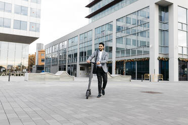 Casual young businessman pushing electric scooter in the city - JRFF03971