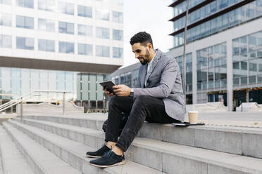 Casual young businessman sitting on stairs in the city using tablet - JRFF03973