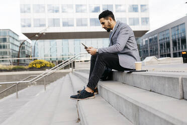 Lässiger junger Geschäftsmann sitzt auf einer Treppe in der Stadt und benutzt ein Tablet - JRFF03976