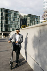 Casual young businessman pushing electric scooter in the city - JRFF03985